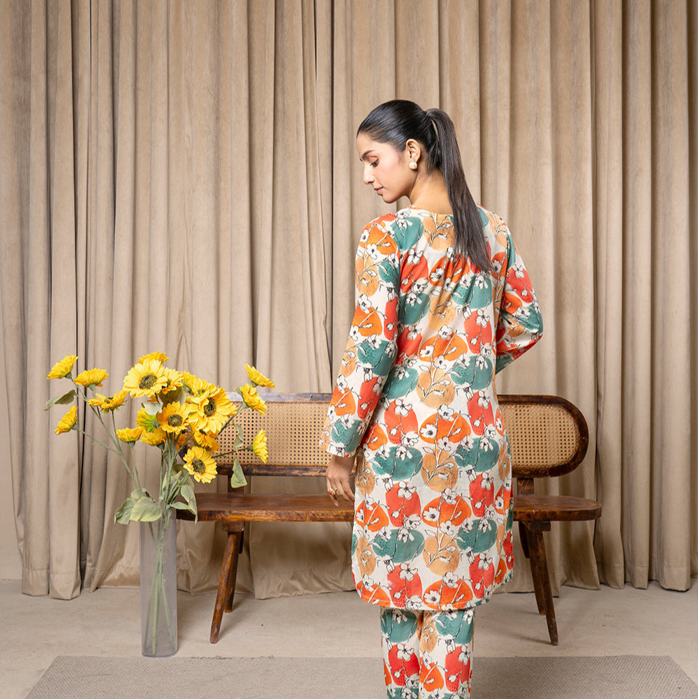 Woman in a colorful outfit standing in a room with curtains and a vase of flowers.